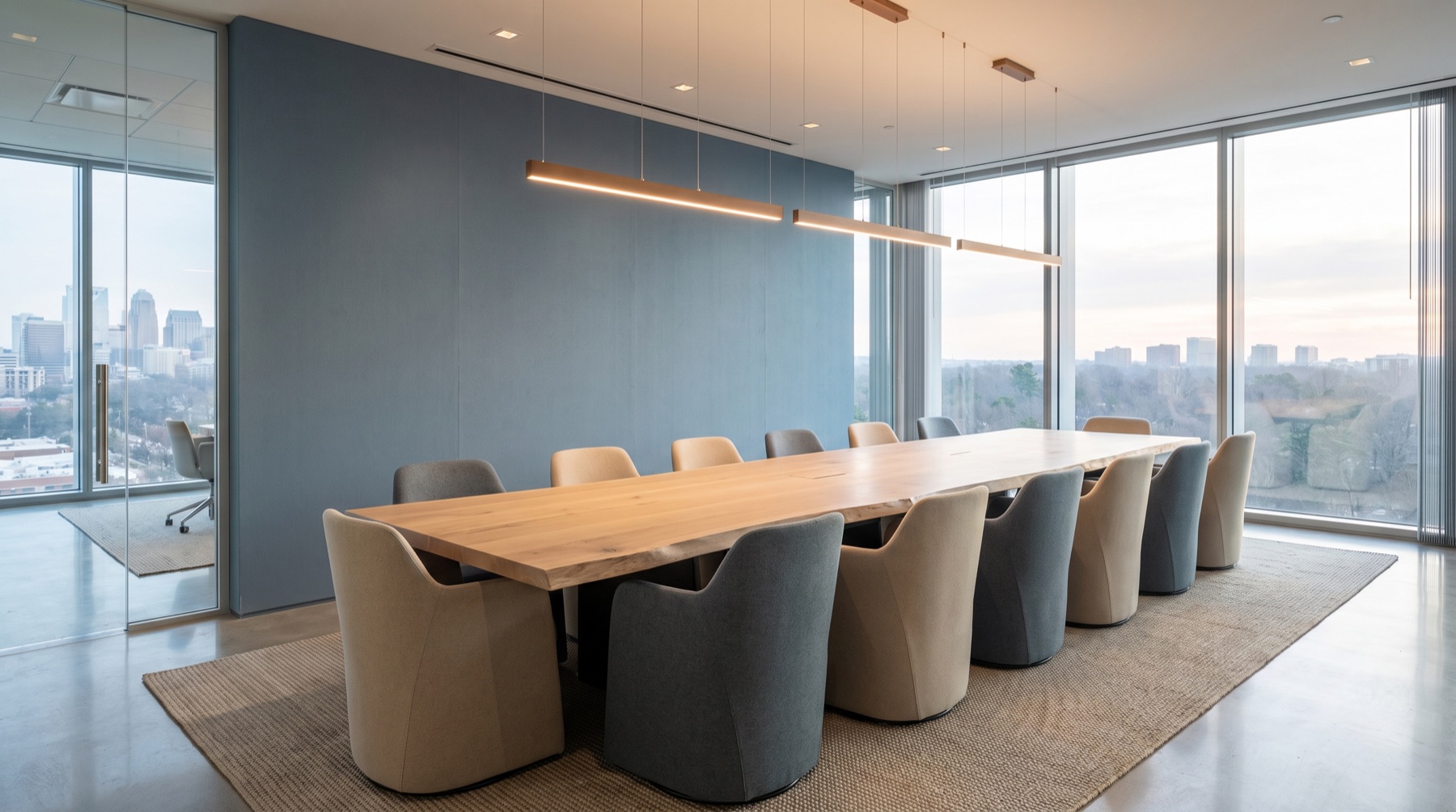 A modern conference room with a white-oak boardroom table, sand and slate upholstered chairs, and a steel-blue accent wall overlooking a city.