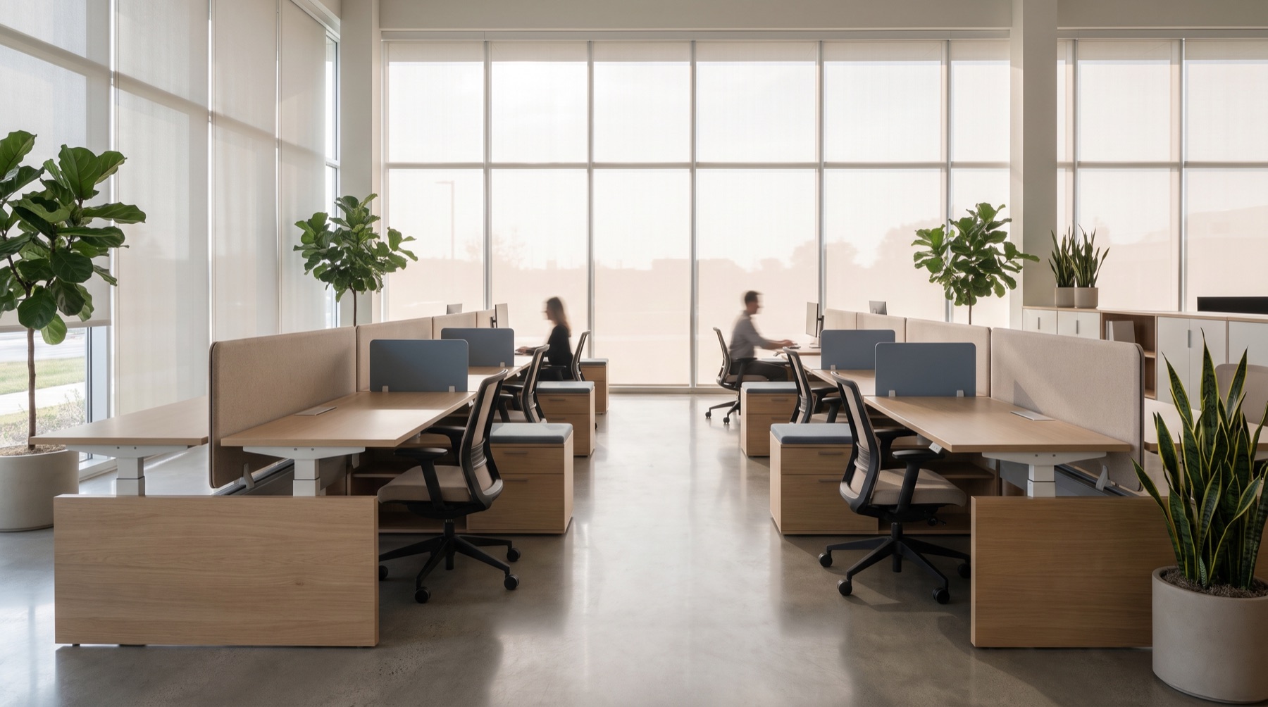 A modern open-plan office furnished with sit-stand benching workstations, oak surfaces, and sand and steel-blue acoustic screens, lit by floor-to-ceiling windows.